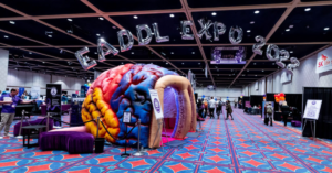 A photo of the expo. There is a large, inflated reproduction of the brain at the front, several tables, and baloons.