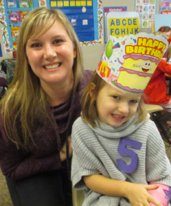 A mother and child smile for a photo while celebrating the girl's 5th birthday.