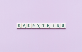 The image shows the word "EVERYTHING" spelled out using Scrabble-like letter tiles. Each tile features a letter with a corresponding point value. The tiles are arranged in a straight line on a soft lavender background.