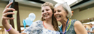 A young girl taking a selfie with her grandmother. They are both smiling and looking at the phone.