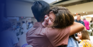 A young man and a woman hugging. She is smiling. They are at a conference.