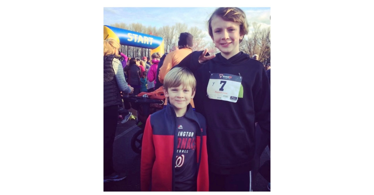 Two boys standing. They are smiling. One is older than the other.